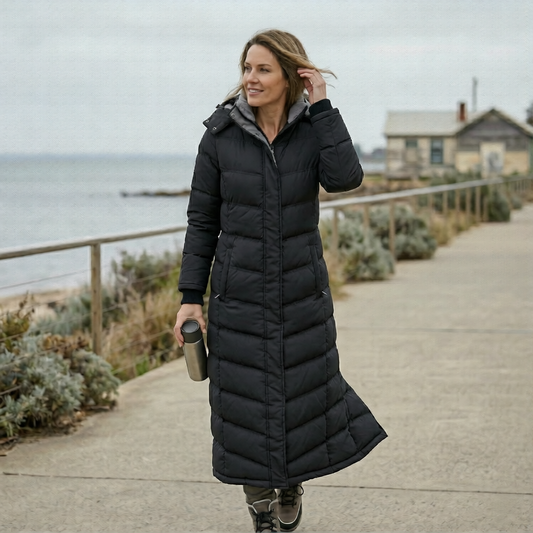 Woman in a long black puffer coat walking along a coastal path.