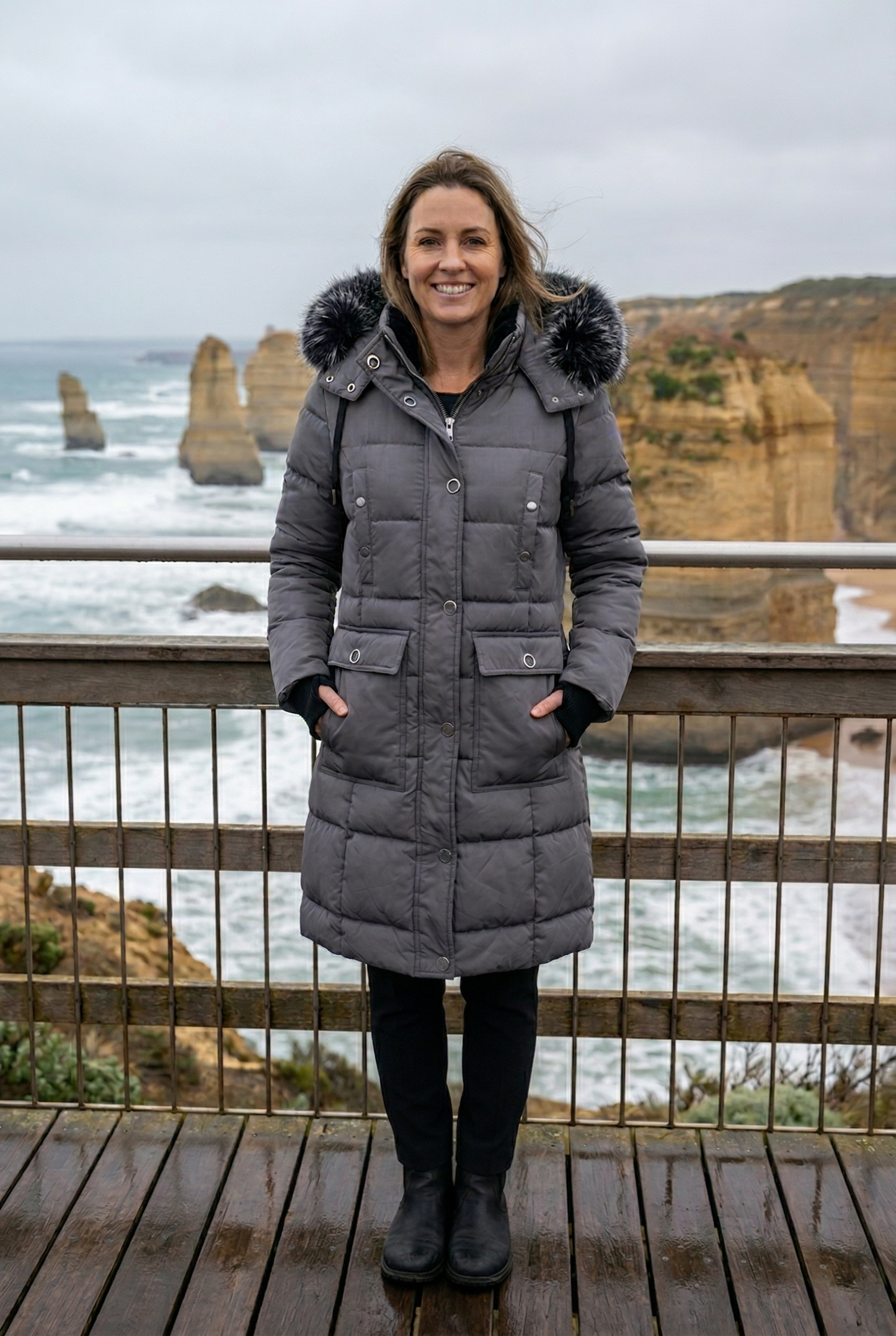 Woman in a gray parka standing in front of ocean cliffs.