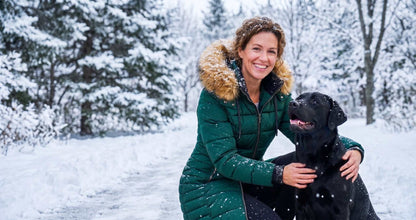 AI lifestyle illustration of a woman crouching beside a black Labrador in snow, wearing the Hunter Green ELORA 7609-8 parka.
