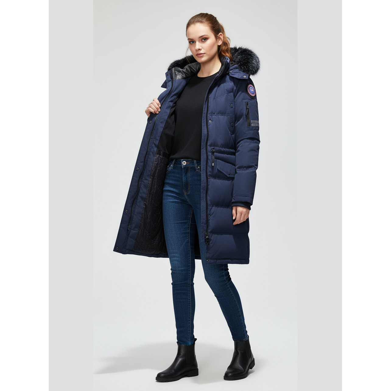 Woman wearing a long navy blue puffer coat with fur hood on a white background