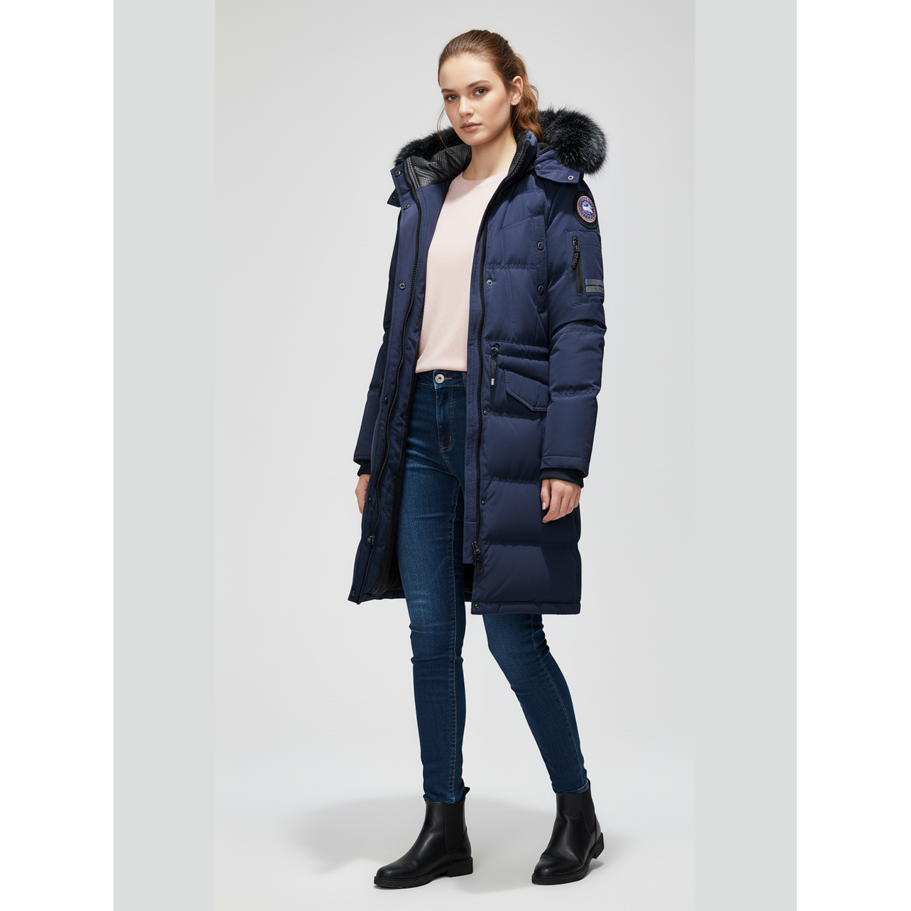 Woman wearing a long navy blue puffer coat with fur hood on a white background