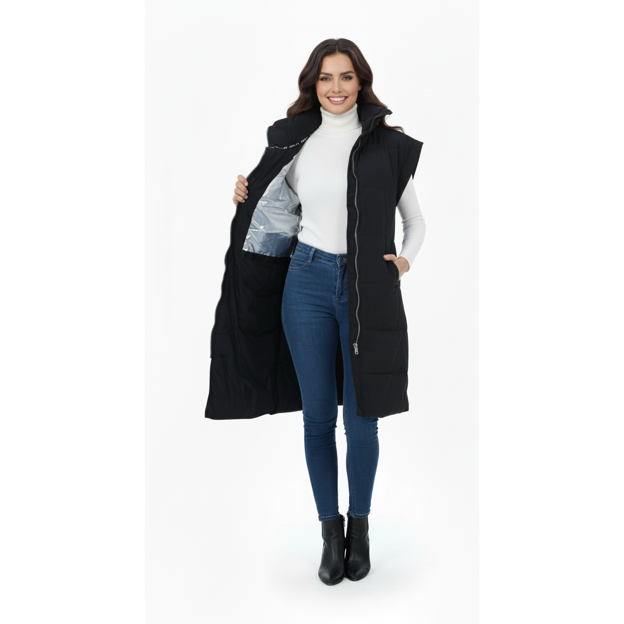 Woman wearing a long black puffer vest over a white turtleneck and blue jeans on a white background