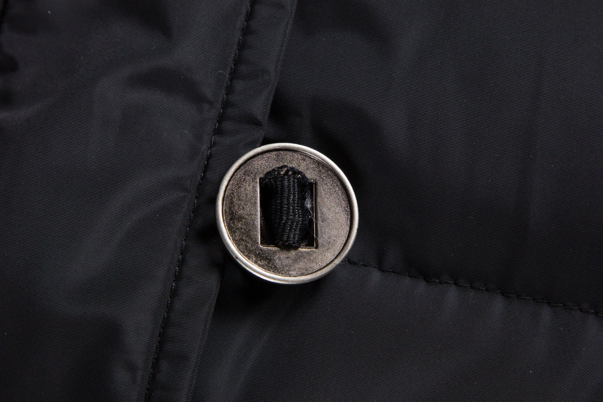 Close-up of the round metal button and fabric attachment on the black ELORA 2566 parka.